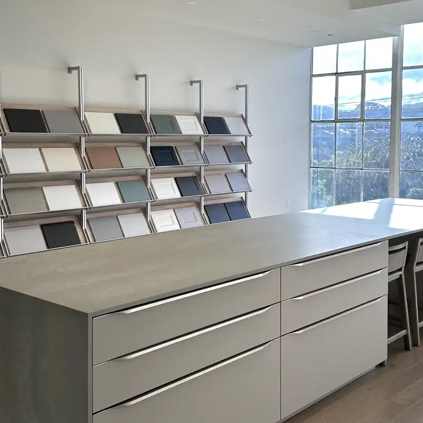 Interior of the FORM studio in San Francisco, characterized by its spacious and bright design. The room features expansive windows that fill the space with natural light, highlighting the light wooden floors and modern furnishings. A central island with a neutral counter finish is complemented by wall-mounted shelving with various design samples and sleek cabinetry. The word 'FORM' in bold letters adorns the far wall, enhancing the room’s modern and professional atmosphere.