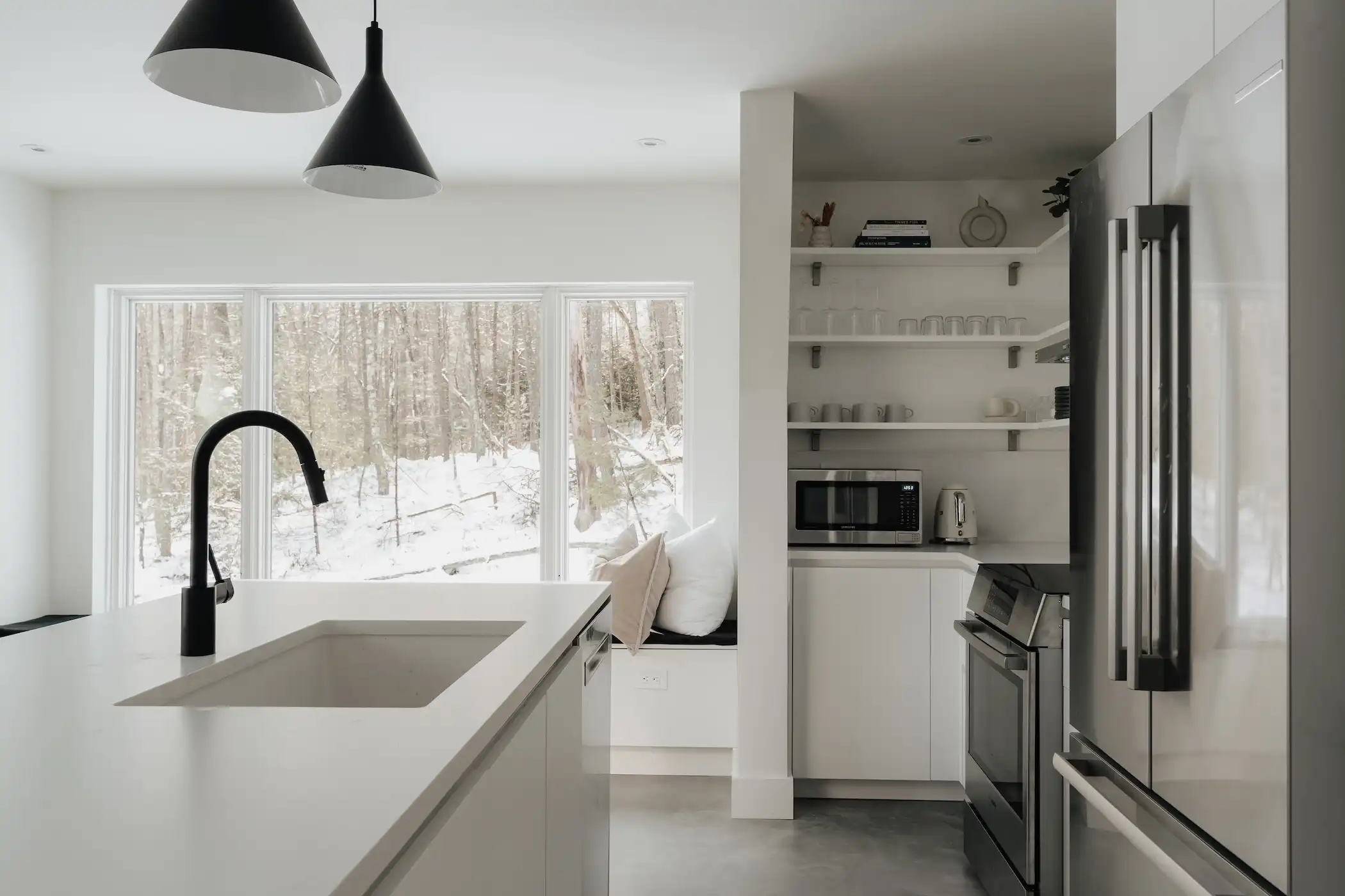 Modern and minimalist kitchen design with clean white cabinetry and an island with a white countertop and contrasting black faucet. 