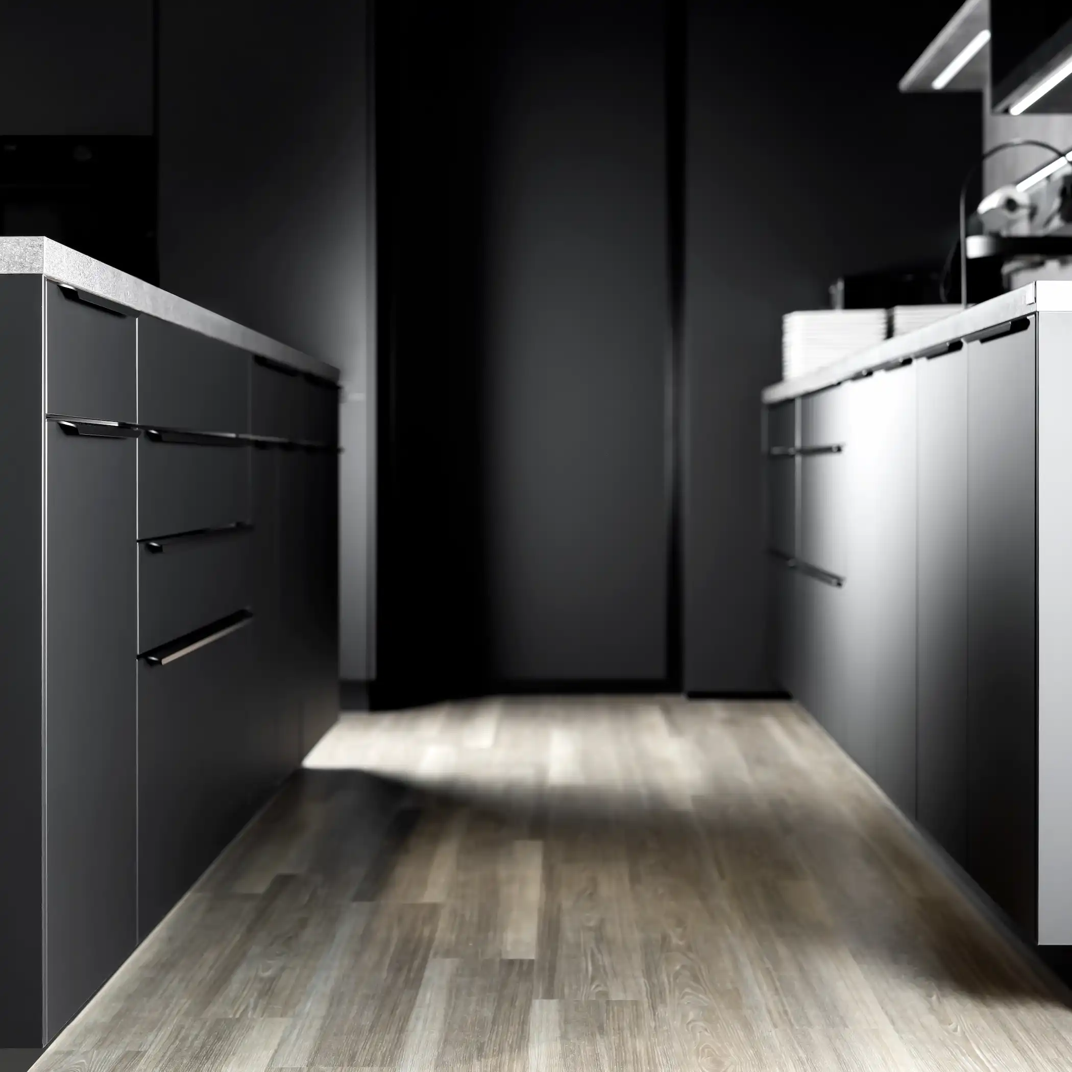 Modern double galley kitchen featuring contrasting dark and light cabinetry. The flat-front cabinets feature integrated handles, enhancing their sleek design. The floor is laid in light wooden planks, adding warmth to the dramatic, contemporary aesthetic of the space.