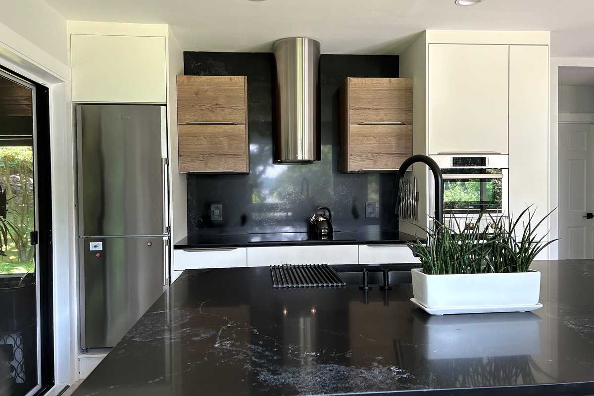 A sleek, contemporary kitchen featuring a mix of white and wood cabinetry. The design includes a black countertop and backsplash, complemented by stainless steel appliances, including a built-in oven and microwave.