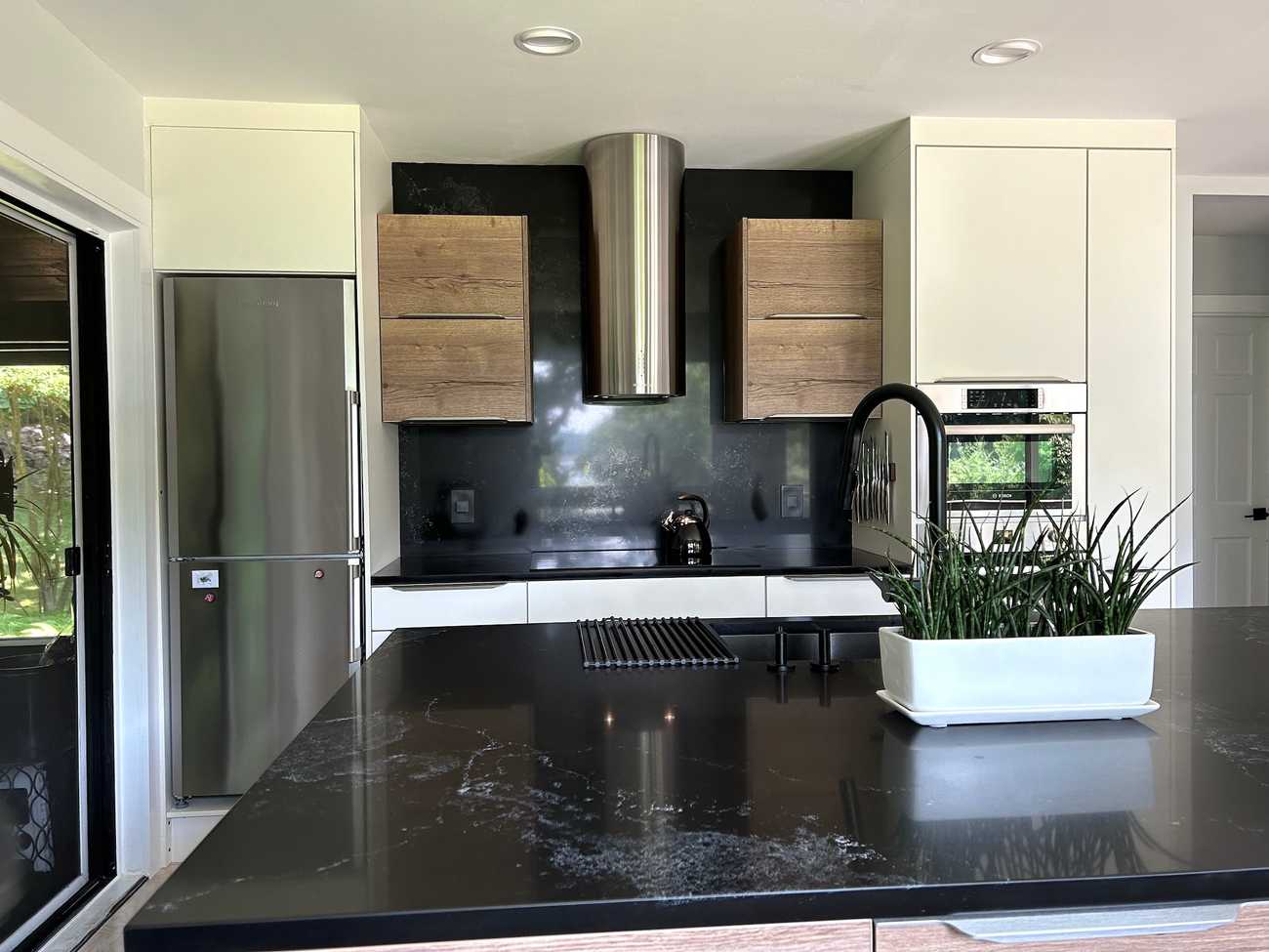 A sleek, contemporary kitchen featuring a mix of white and wood cabinetry. The design includes a black countertop and backsplash, complemented by stainless steel appliances, including a built-in oven and microwave.