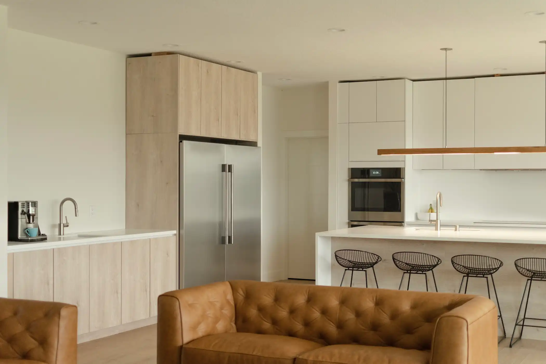 Contemporary kitchen bathed in natural light, showcasing a large white island with sleek bar stools and a harmonious blend of white cabinetry and our Oak Montreal cabinets.